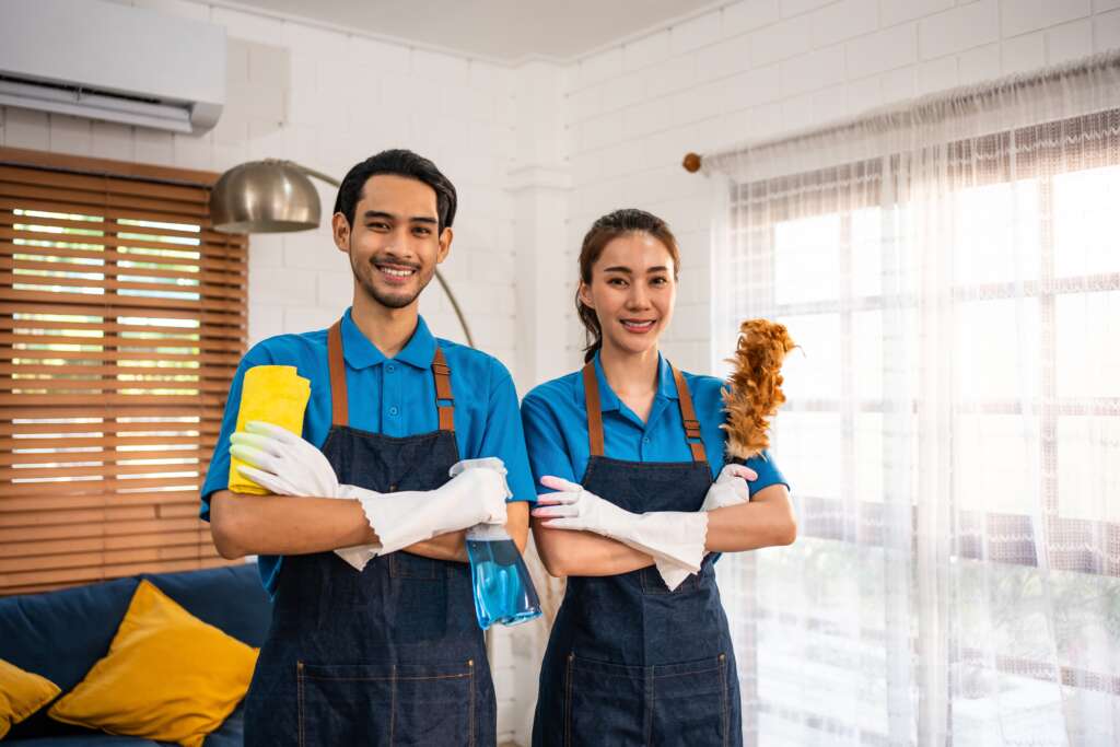 two helpers smiling while holding cleaning supplies