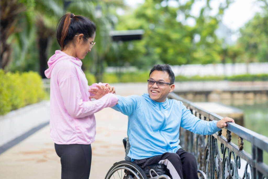 Caregiver assisting a wheelchair user outdoors, highlighting disability care support arranged through the best maid agency in Singapore