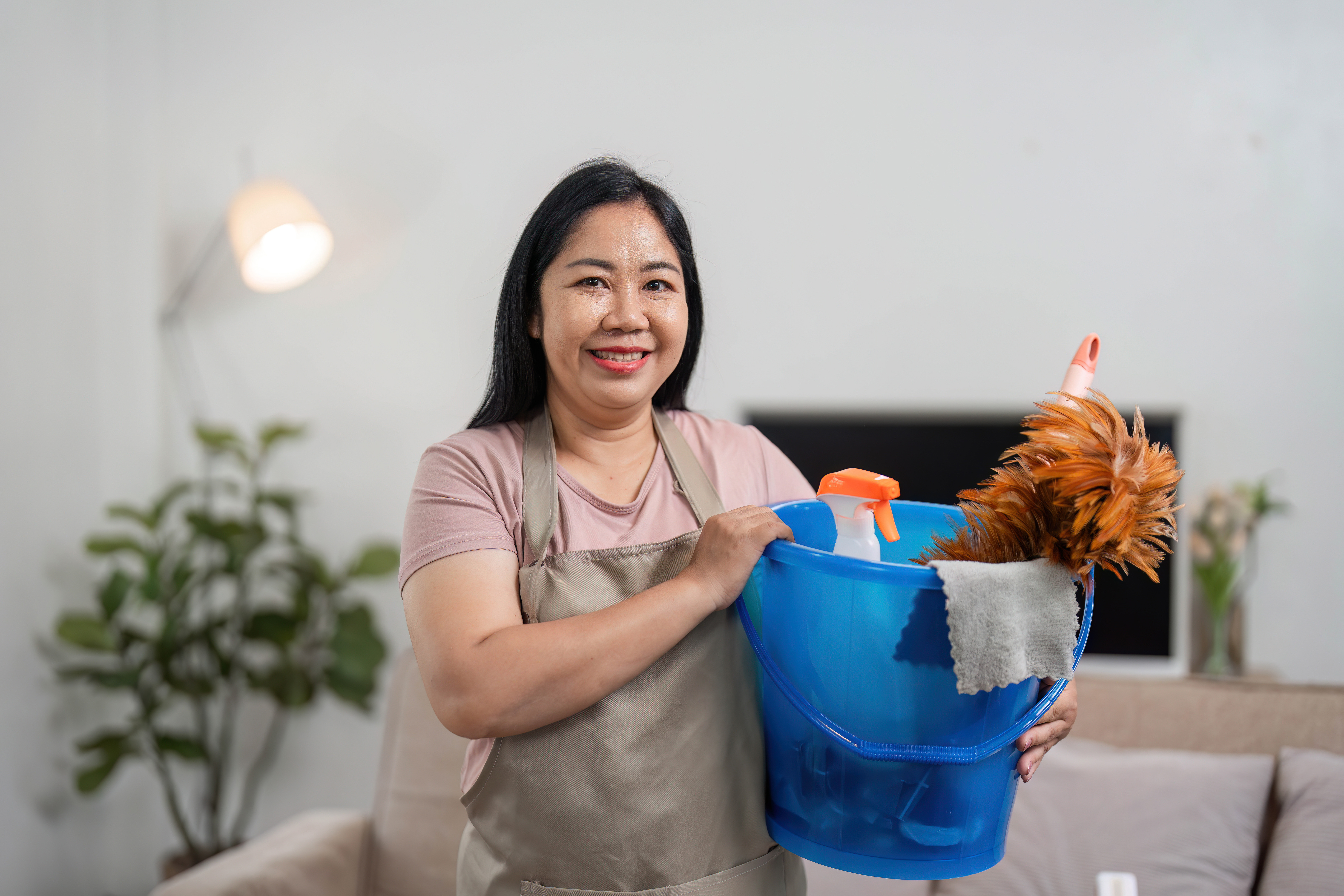 Filipino domestic helper holding cleaning supplies, representing services provided by a filipino maid agency in Singapore